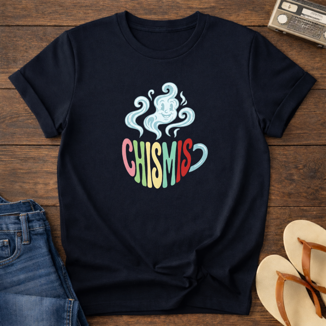 Navy blue t-shirt with colorful 'CHISMIS' design on a wooden surface with jeans and a hat.